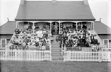 Crowd sitting in front of cricket pavilion, Savile Town, Dewsbury