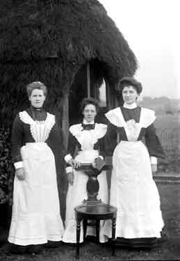 Domestic servants outside thatched cottage