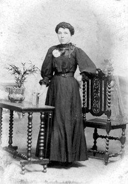 Portrait of a woman standing between a table and chair - Aunt Rosie Bean.