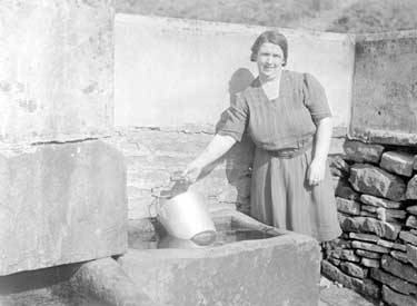 Woman fetching water from trough 	