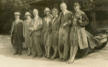 "Cloche" hats - Group of people standing in front of a vehicle.