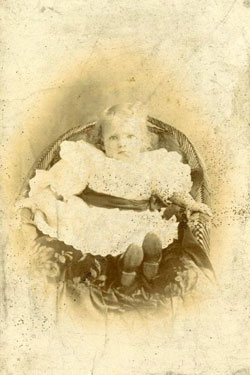 Portrait of a small child (girl) sat in a basket weave chair.