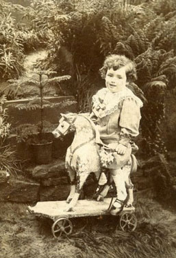 Portrait of a young boy, sat on a wooden horse.