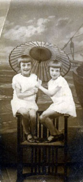 Portrait of a two young girls sat under a parasol.