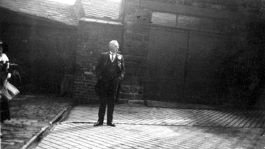 Man standing in yard, wearing a suit with button hole.