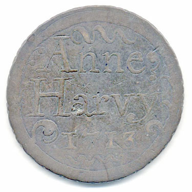 A bronze halfpenny coin which has been polished on both sides in order to produce a love token; on one side is the name Anne Harvy with the date 1713, on the other a faint floral design.