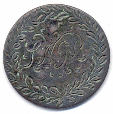 A bronze halfpenny (probably) coin which has been smoothed to make a love token; one side has the interlocked SWGS (probably); the other side has an ornamental flower basket design.