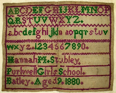 An unframed sampler signed Hannah M. Stubley of Purlwell Girls' School, Batley, 1880. A small cross-stitch sampler featuring the alphabet and single numbers in green and pink on coarse backing.