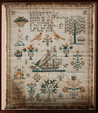 A framed sampler signed Harriet Fell, aged 12. Elaborate design, religious text, central motif of ship with black sailors or slaves?, trees, birds, flowers and simple border.