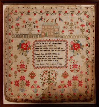 A framed sampler signed Lydia Booth, 1834. Elaborate design with religious motto in centre, Adam and Eve, the Tree of Life, serpent, birds, flowers, house and border of strawberries.