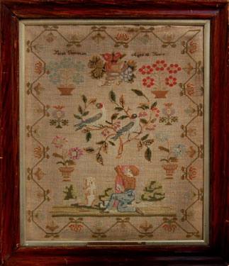 A framed sampler signed Sarah Thornton, aged 10. Elaborate design including, kneeling boy, dog, 2 birds on a branch, flowers, surrounded by flower border. In cross stitch.