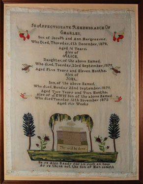 A framed sampler created in remembrance of four of the children of Joseph and Ann Hargreaves. Angels, birds above a fenced tomb surrounded by trees; with religious text