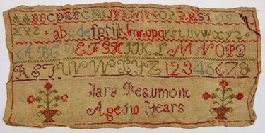 An unframed sampler signed Clara Beaumont, aged 10; with alphabet, numbers and two baskets of flowers.