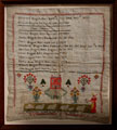 View: ksp00029 A framed sampler signed Sarah Hague, 1834. Memorial to Edward Hague and Hannah Hague and their ten children. Includes picture of a house, flowers, shepherdess and flock of sheep, with floral border.