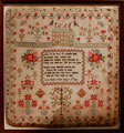View: ksp00033 A framed sampler signed Lydia Booth, 1834. Elaborate design with religious motto in centre, Adam and Eve, the Tree of Life, serpent, birds, flowers, house and border of strawberries.